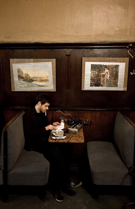 Musiker Effi sitzt in einem Kaffeehaus, am Tisch ein elektronisches Gerät neben Kaffeehäferl und Kopfhörern.